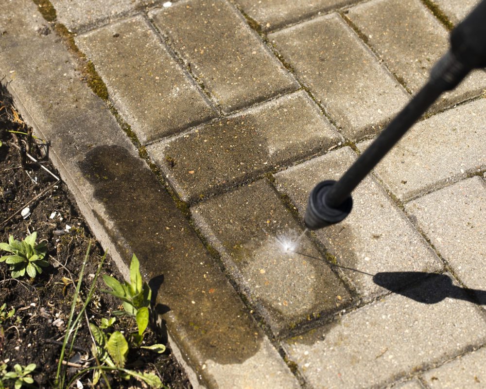 sprayer of high-pressure washer cleans concrete stones of garden line in country house Spring cleaning concept natural resources saving concept